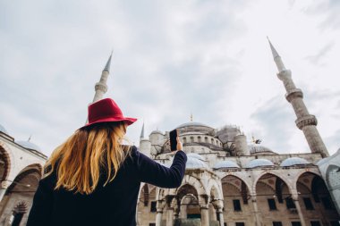 Genç Avrupalı kadın İstanbul, Türkiye 'de selfie portresi çekiyor. Kız kış İstanbul 'unda yürüyor. Sarışın, sonbahar günü bir caminin arka planında telefonla fotoğraf çekiyor..