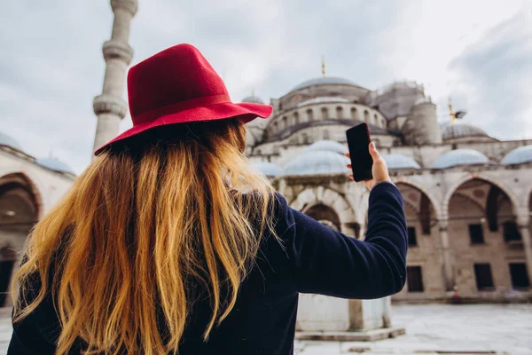 Genç Avrupalı kadın İstanbul, Türkiye 'de selfie portresi çekiyor. Kız kış İstanbul 'unda yürüyor. Sarışın, sonbahar günü bir caminin arka planında telefonla fotoğraf çekiyor..