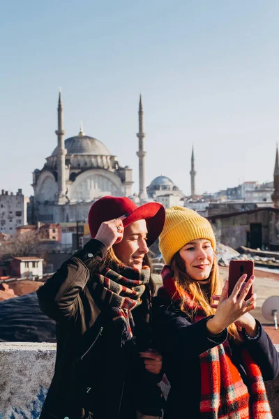 Kız arkadaşlar, İstanbul, Türkiye 'deki Grand Bazaar' ın çatısında selfie çekiyorlar. Açık bir kış gününde İstanbul 'un arka planında iki gülümseyen kız telefonla fotoğraflanıyor.
