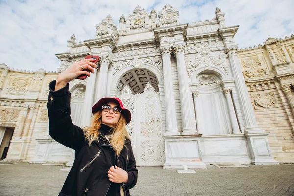 Kız, Dolmabahce, İstanbul, Türkiye 'nin önündeki meydanda selfie çekiyor. İstanbul 'da Sultan' ın Sarayı önünde şapkalı ve paltolu genç bir kızın fotoğrafı çekiliyor..