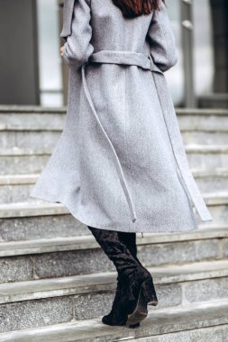 Açık havada ceketli bir kız. Dış giyim mankeni. Uzun gri montlu esmer, şehrin etrafında yürüyor. Şık bir manto içinde güzel bir kız. bahar sonbahar koleksiyonu.