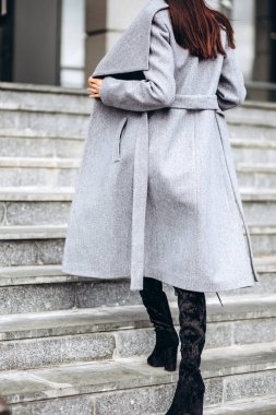 Açık havada ceketli bir kız. Dış giyim mankeni. Uzun gri montlu esmer, şehrin etrafında yürüyor. Şık bir manto içinde güzel bir kız. bahar sonbahar koleksiyonu.