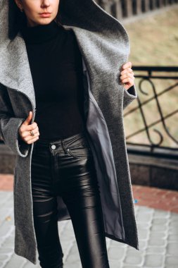 Açık havada ceketli bir kız. Dış giyim mankeni. Uzun gri paltolu bir esmer nehrin seti boyunca yürüyor. Şık bir manto içinde güzel bir kız. bahar sonbahar koleksiyonu.