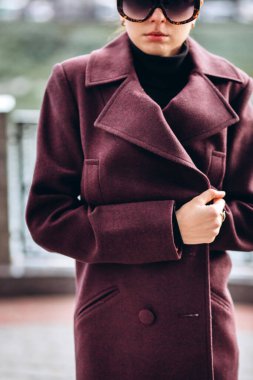 Açık havada ceketli bir kız. Dış giyim mankeni. Uzun bordo paltolu bir esmer nehrin seti boyunca yürür. Şık bir manto içinde güzel bir kız. bahar sonbahar koleksiyonu.