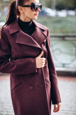 Açık havada ceketli bir kız. Dış giyim mankeni. Uzun bordo paltolu bir esmer nehrin seti boyunca yürür. Şık bir manto içinde güzel bir kız. bahar sonbahar koleksiyonu.