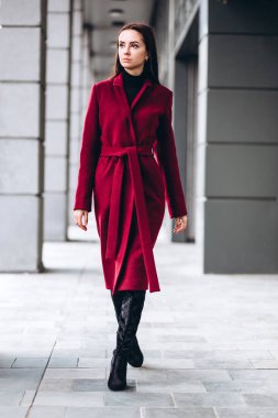 Açık havada kalın ceketli bir kız. Dış giyim mankeni. Uzun kırmızı paltolu esmer şehrin etrafında yürüyor. Şık bir manto içinde güzel bir kız. bahar sonbahar koleksiyonu.