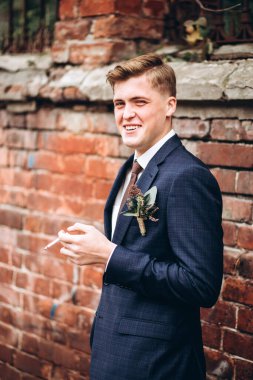 Takım elbiseli ve kravatlı vahşi damat sigara içiyor. Sarışın adam eski kasabada geziniyor. Sigara, kötü alışkanlıklar. Duvarın arkasında genç bir iş adamı var. Gülümseyen bir adam portosu..