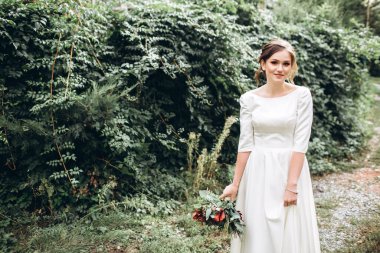 Mütevazı bir elbise içindeki güzel bir gelinin portresi. Uzun kollu, beyaz elbiseli esmer kız. Sonbahar buketi olan tatlı bir gelin. Bir sonbahar sokağında açık havada bir kadının portresi..