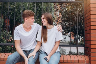 Sonbahar günü şehirde yürüyen genç bir çift. Mutlu bir çift tuğla bir çitte oturuyor ve gülüyor. Gerçek duygular. Yakın plan bir çift portre. Güneşli bir günde bir erkek ve bir kadın dışarı çıkar..