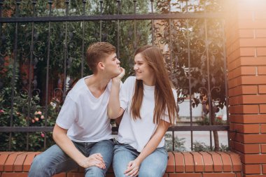 Sonbahar günü şehirde yürüyen genç bir çift. Mutlu bir çift tuğla bir çitte oturuyor ve gülüyor. Gerçek duygular. Yakın plan bir çift portre. Güneşli bir günde bir erkek ve bir kadın dışarı çıkar..