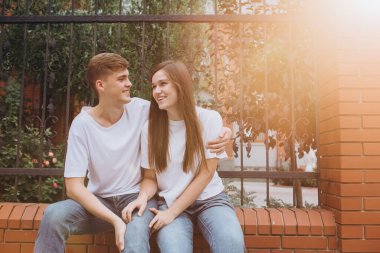 Sonbahar günü şehirde yürüyen genç bir çift. Mutlu bir çift tuğla bir çitte oturuyor ve gülüyor. Gerçek duygular. Yakın plan bir çift portre. Güneşli bir günde bir erkek ve bir kadın dışarı çıkar..