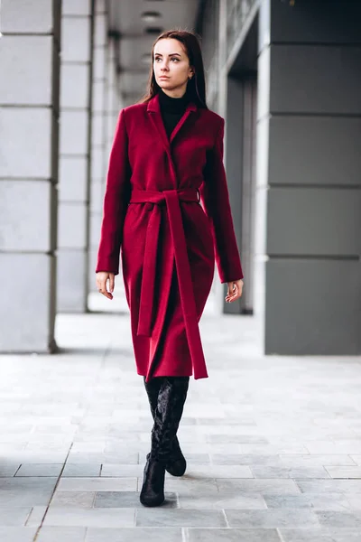 girl in a warm light coat outdoors. model in outerwear. brunette in a long red coat walks around the city. beautiful girl in a fashionable casual coat. spring autumn collection.