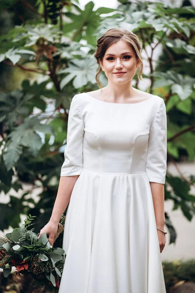 Mütevazı bir elbise içindeki güzel bir gelinin portresi. Uzun kollu, beyaz elbiseli esmer kız. Sonbahar buketi olan tatlı bir gelin. Bir sonbahar sokağında açık havada bir kadının portresi..