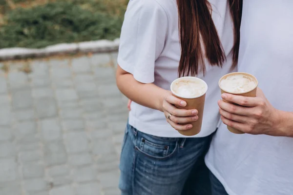 부부는 도시의 거리를 거닐면서 판지로 잔에서 커피를 마십니다 티셔츠를 야외에서 — 스톡 사진