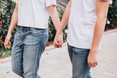 Mutlu genç çift şehrin sokaklarında yürüyor ve el ele tutuşuyorlar. Beyaz tişörtlü erkek ve kız açık havada kot pantolon giyiyor. Gençler sonbahar şehrinde duvarın arkasında yürüyorlar..