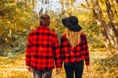 Genç çift sonbahar ormanında el ele tutuşarak yürüyor. Güzel giyimli bir erkek ve kız. Adam ve kırmızı ceketli kız sarı ormanın arka planında. Parkta aşık mutlu genç bir çift