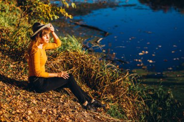 Gri şapkalı bir sarışın sonbahar ormanında yürüyor. Sarı kazaklı neşeli bir kız güneşli bir sonbahar gününde gölün kenarında oturur. Ormanda yürüyen bir kadın.