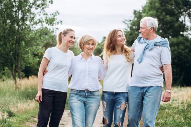 Yetişkin kızları olan yaşlı bir çift doğada yürür. Olgun bir çift ormanda yürüyor. Beyaz tişörtlü ve kot pantolonlu bir aile parkta yürüyor. Mutlu bir aile. Aile dışarıda iletişim kurar.