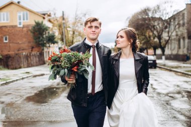 Genç mutlu çift yağmurdan sonra bir şehir caddesinde yürüyor. Bir erkek ve kadının yakın plan portresi. Dışarıda gülümseyen sevimli bir çift. Şehirde güneşli bir sonbahar günü.