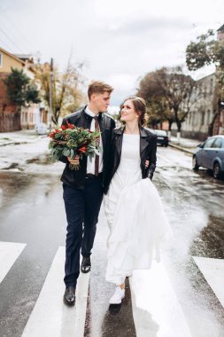 Genç mutlu çift yağmurdan sonra bir şehir caddesinde yürüyor. Bir erkek ve kadının yakın plan portresi. Dışarıda gülümseyen sevimli bir çift. Şehirde güneşli bir sonbahar günü.