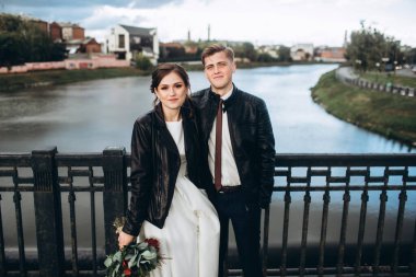 Genç bir çift nehrin üzerindeki köprüde sarılıyor. Deri ceketli gelin ve damat. Soğuk bir sonbahar gününde şehirde gezen sevgi dolu bir çift. Fırtınalı gökyüzü ile şehrin panoraması