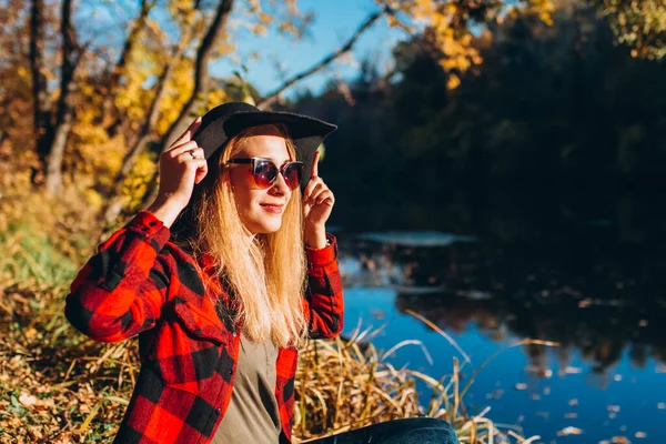 Gri şapkalı bir sarışın sonbahar ormanında yürüyor. Kırmızı ceketli neşeli kız güneşli bir sonbahar gününde gölde oturur. Ormanda yürüyen bir kadın.