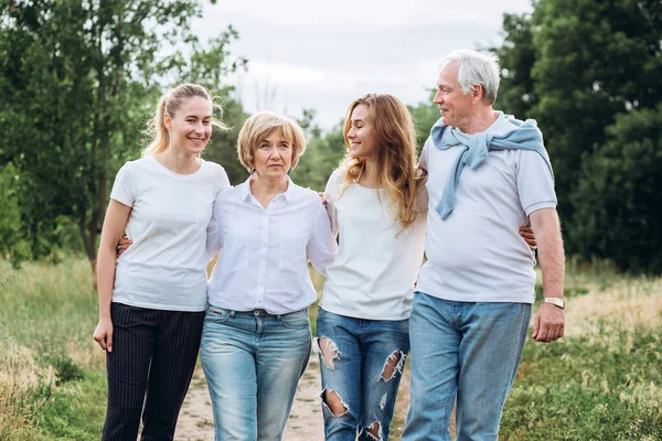 An elderly couple walks with adult daughters in nature. Mature couple walks in the woods. A family in white t-shirts and jeans is walking in the park. Happy family. family communicates outdoors
