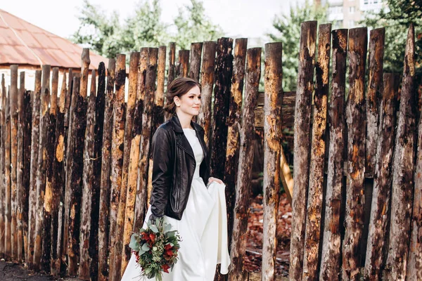 Mütevazı bir elbise içindeki güzel bir gelinin portresi. Uzun kollu, beyaz elbiseli esmer kız. Sonbahar buketi olan tatlı bir gelin. Bir sonbahar sokağında açık havada bir kadının portresi..