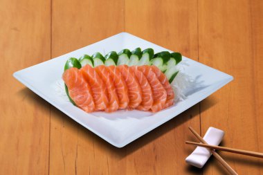 SALMON SASHIMI 'NİN Dilimleri, beyaz bir tabakta sunuldu, tahtanın arka bahçesinde.