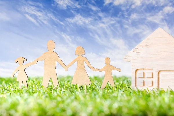 Ahşap aile, güzel gökyüzünün üzerindeki yeşil çimlerde şekillendirilmiş ahşap ev şekilli. Yeşil Aile Konsepti.