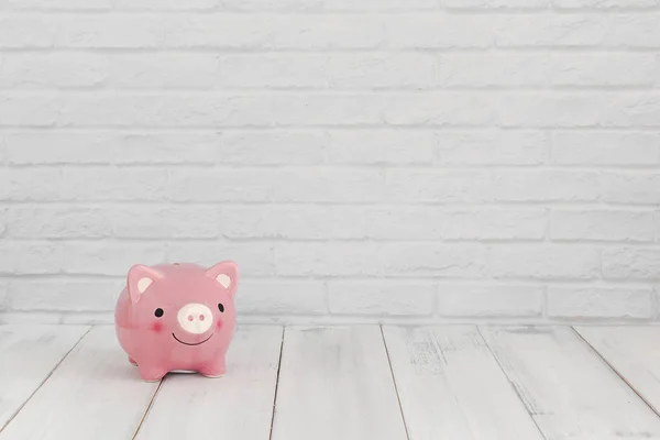 Pink piggy bank on white wood table over white brick background