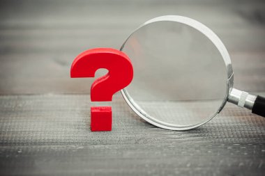 Red Question mark with magnifying glass on wood table