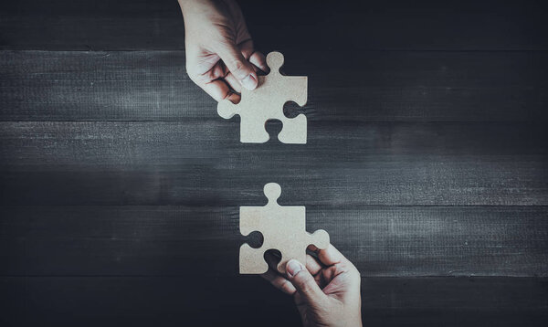 Two hands holding wooden jigsaw puzzle pieces and solving put pi