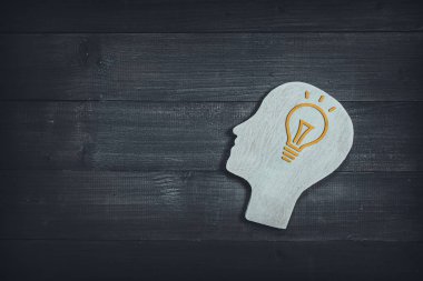 Ahşap masa sırtında ampul işareti olan insan kafası ve yüzü.