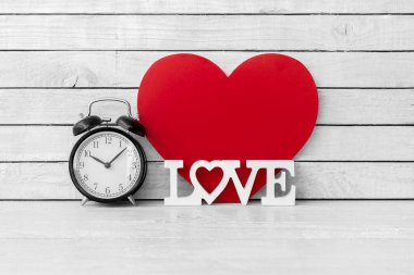 Aşk alfabesi ve beyaz ahşap zemin üzerinde kırmızı kalp şekillendirilmiş çalar saat.