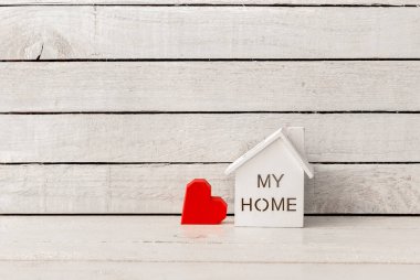 Evim beyaz ahşap arka planda kırmızı kağıt bir kalple şekillendi..