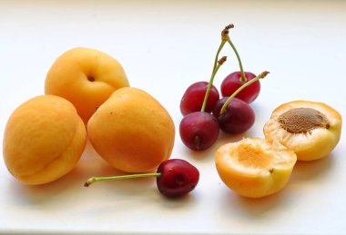 Kayısı taze, olgun. Çok tatlı. Beyaz bir zemin üzerinde, kırmızı kiraz ağacının meyveleriyle birlikte, hoş kokulu. Hayat yazdır..