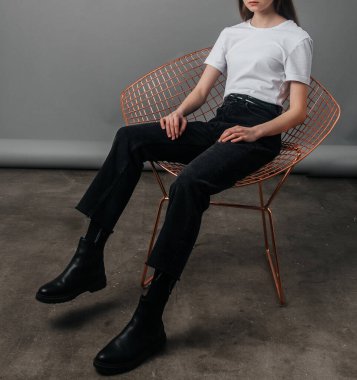 Poz veriyor. Siyah kotla poz veren yüksek bel, kemer ve beyaz tişört giyen bir manken. Poz verme dersleri. Stüdyoda fotoğraf çekimi. Kadın pozu