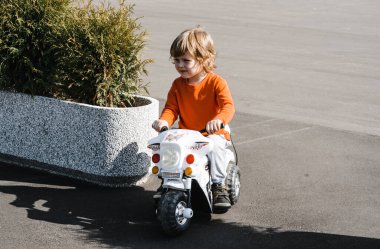 Çocuk asfalt bir yolda oyuncak bir motosiklete biniyor. Çocuk temiz hava aktivitelerinde yürüyüşe çıktı..