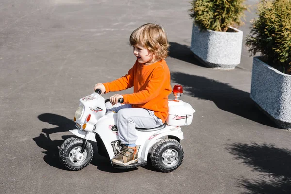 Çocuk asfalt bir yolda oyuncak bir motosiklete biniyor. Çocuk temiz hava aktivitelerinde yürüyüşe çıktı..