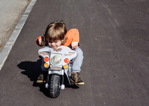 少年はアスファルトの道路で子供のおもちゃのバイクに乗っています。新鮮な空気の屋外活動の中を歩く子供は. — ストック写真