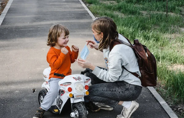 Anya felvesz egy orvosi védőmaszkot egy sétáló gyereknek. Koronavírus-világjárvány elleni védelem — Stock Fotó