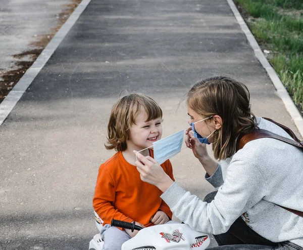 Mamma tar på sig en medicinsk skyddsmask för ett barn på en promenad. Skydd mot en coronaviruspandemi — Stockfoto