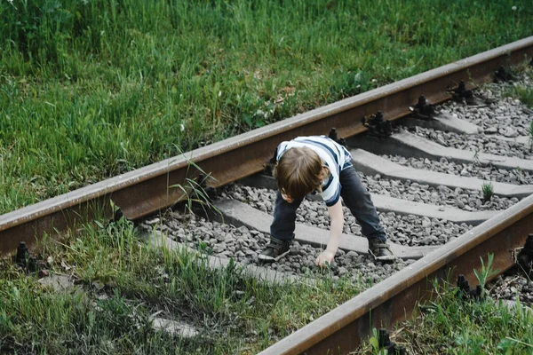 curly-haired boy in a striped T-shirt walks on rails. railway, danger
