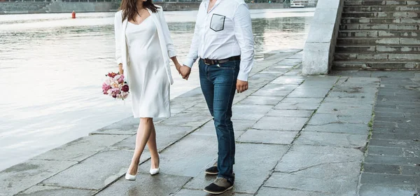 pregnant bride in a thin white dress on thin spaghetti straps with bare shoulders with a bouquet of peonies