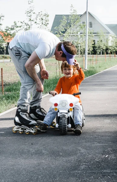 father and son for a walk. boy on a toy children motorcycle dad roller skate. family holiday. father day