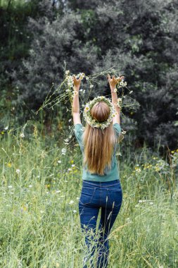 Kafasında uzun saçlı bir çelenk olan genç bir kadın arkasında duruyor ve bir buket kır çiçeği fırlatıyor. 