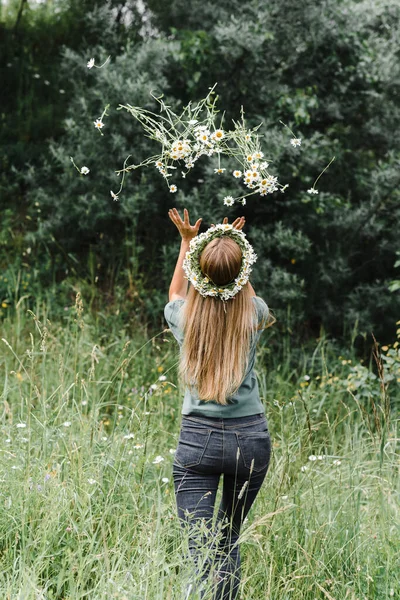 Une jeune femme dans une couronne sur sa tête avec de longs cheveux se tient avec son dos et vomit un bouquet de fleurs sauvages — Photo