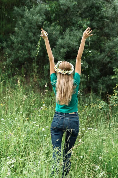 Una joven en una corona en la cabeza con el pelo largo se para con la espalda y arroja un ramo de flores silvestres — Foto de Stock