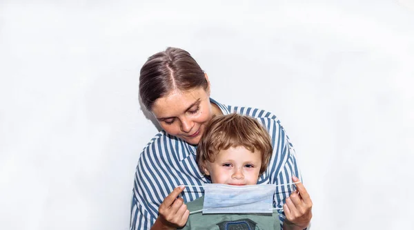 young woman in a blue striped shirt in a medical mask with a baby in her arms. remedy for coronavirus, covid 19,